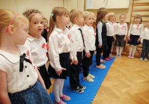 Dzieci stoją na baczność i śpiewają hymn narodowy